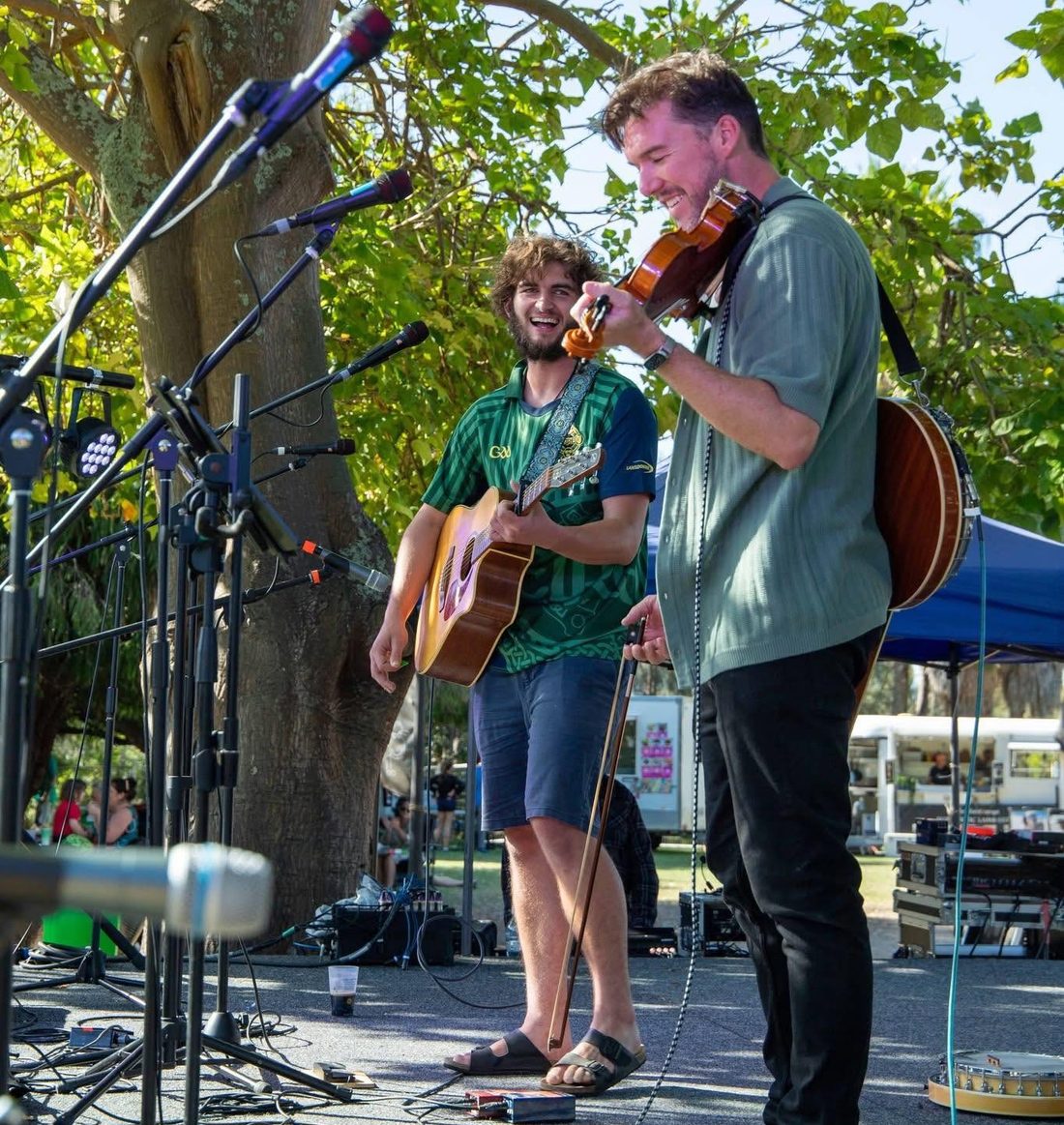 Playing guitar and fiddle outdoors under a tree at the St Patrick&rsquo;s Festival