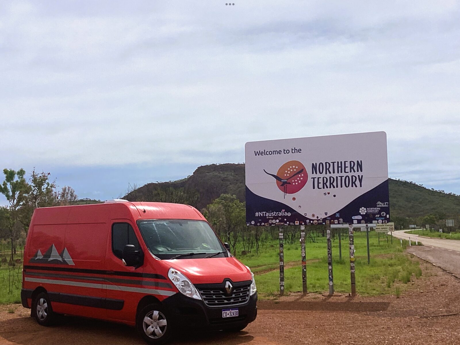 The van parked at the Northern Territory border sign on a red dirt roadside
